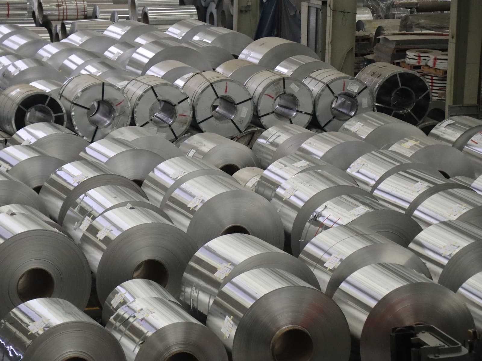Reihen von Metallcoils auf einem Boden, viele mit kleinen Papieretiketten, dahinter umreifte Coils